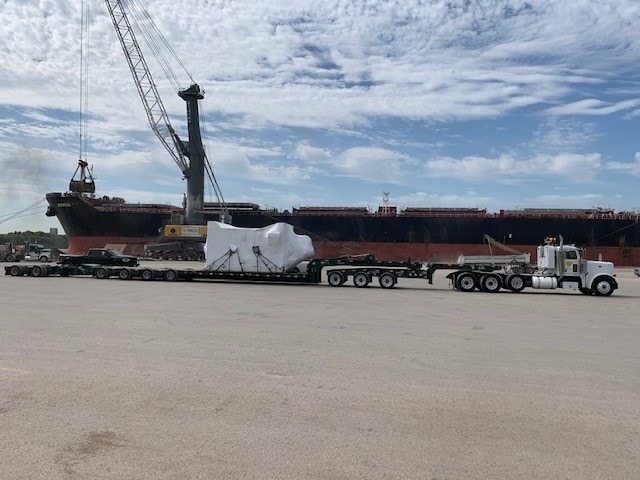 Palletized 13-axle heavy haul load staged at port with ship in background
