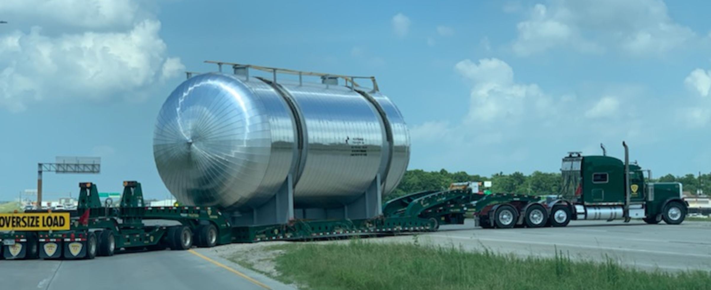 Palletized green Peterbilt hauling twin stainless steel pressure vessels on Cozad lowboy on Texas highway