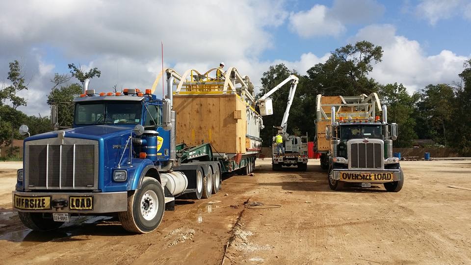 Two Palletized oversize load Peterbilts hauling large crated industrial equipment at a job site