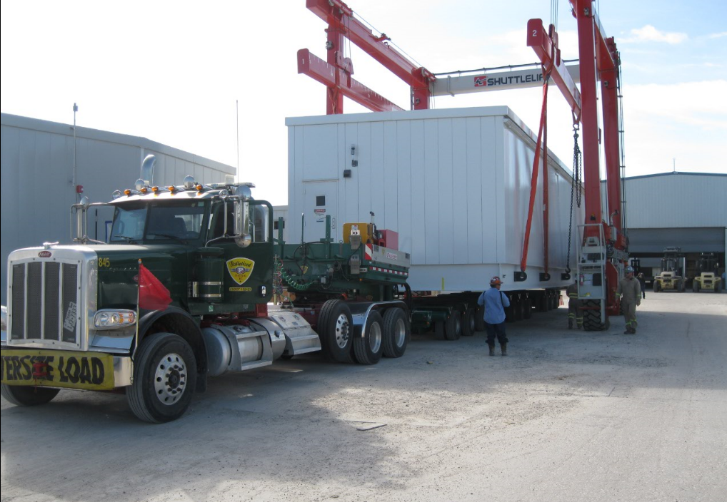 Palletized green Peterbilt oversize load being lifted by Shuttlelift gantry crane at industrial facility