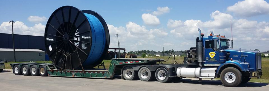 Palletized blue Kenworth hauling large Tenaris cable reel on multi-axle lowboy trailer