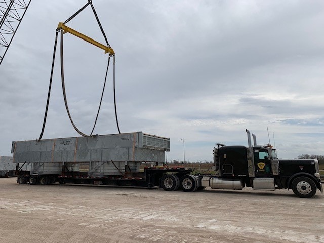 Palletized step deck load being lifted by overhead crane at industrial yard